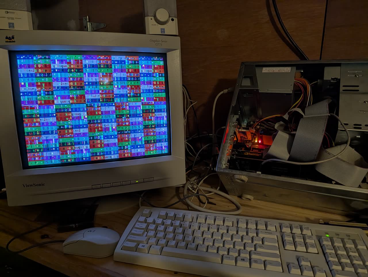 Photograph: 486 CRT monitor showing colorful chaotic patterns of CP437 characters during bench_video text-mode measurement. Open 486 case visible to the right.