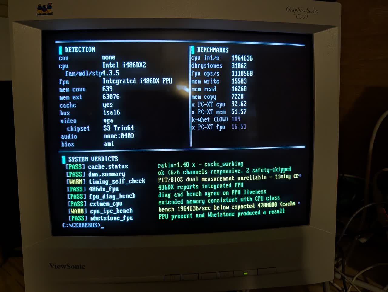 CERBERUS v0.4.0 three-pane UI on a 486 DX-2. Left pane DETECTION lists CPU as Intel i486DX2, FPU as Integrated i486DX FPU, 63,076 KB extended memory, S3 Trio64 video, AMI BIOS. Right pane BENCHMARKS shows 1.96M integer iterations per second, 31,862 Dhrystones, 1.12M FPU ops per second, memory throughput 15 MB per second. Bottom pane SYSTEM VERDICTS lists seven PASS rows and two WARN rows in green and yellow.